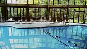 Une grande piscine intérieure à l’eau d’un bleu limpide, entourée de grandes fenêtres et de fauteuils.