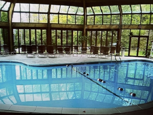 A large indoor swimming pool with clear blue water, surrounded by large windows and chairs.