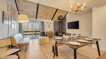 Un espace repas moderne avec une table en bois dressée pour six personnes, un canapé et une grande fenêtre donnant sur un paysage arboré.