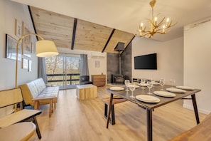 A modern dining area with a wooden table set for six, a sofa, and a large window with a view of trees.
