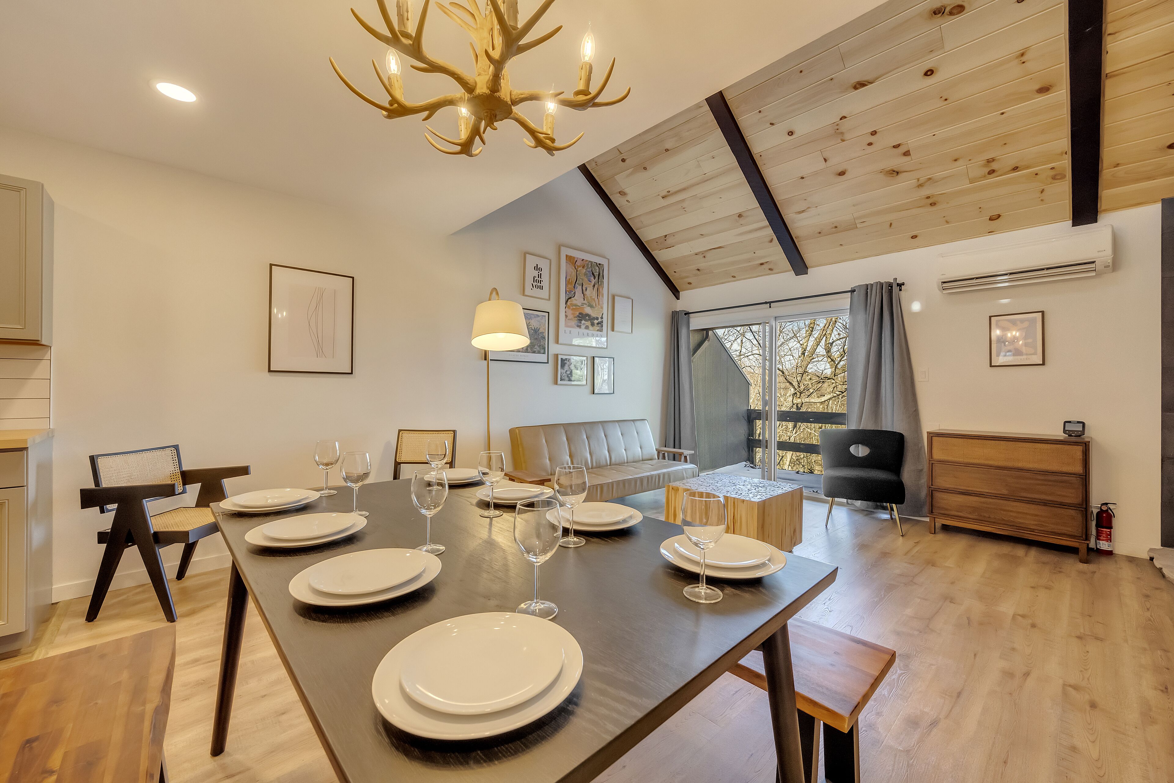 Un espace repas avec une longue table dressée pour six personnes, un lustre et un plafond de style industriel.