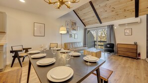 Un espace repas avec une longue table dressée pour six personnes, un lustre et un plafond de style industriel.