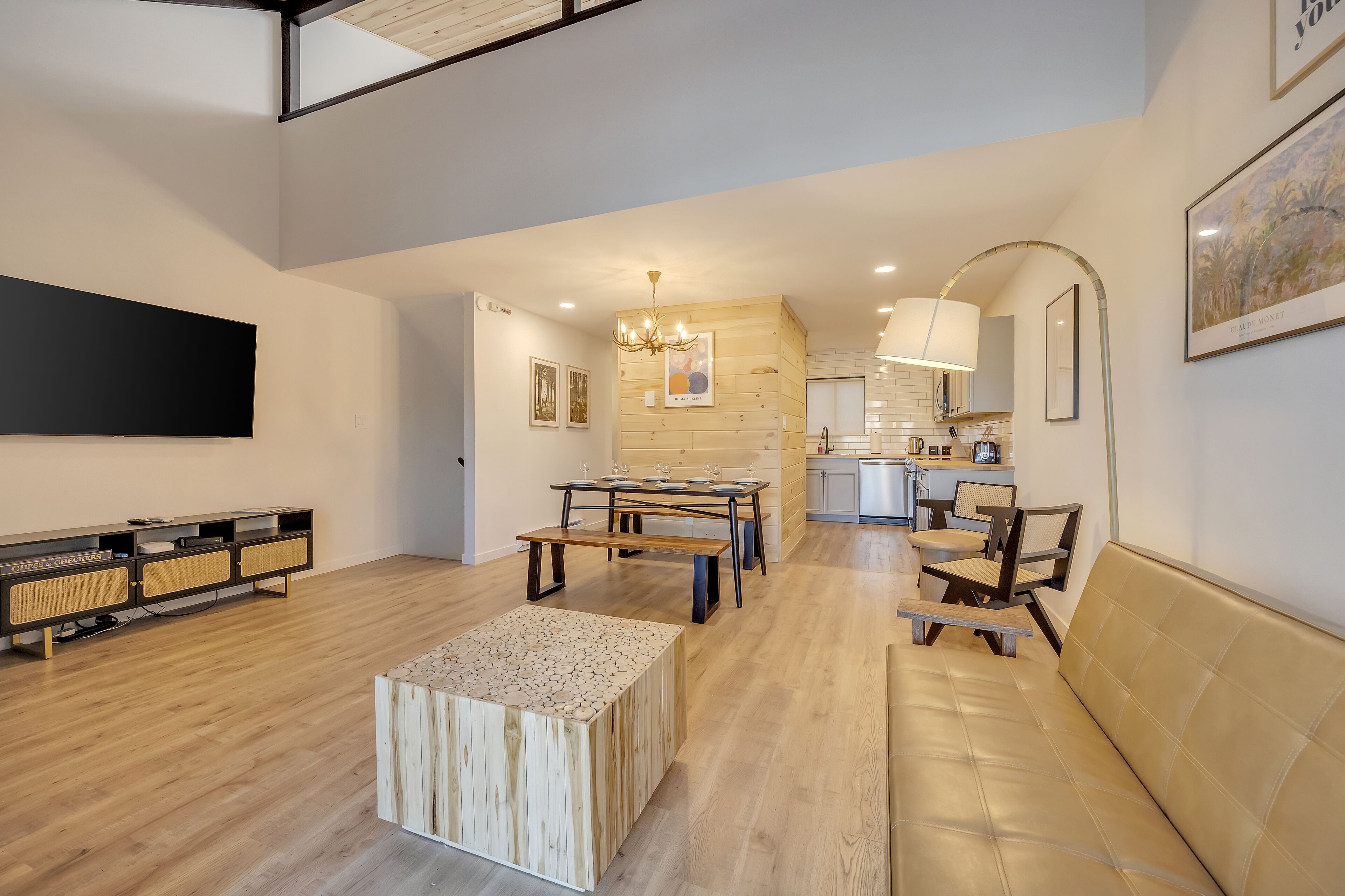 Un vaste espace de vie doté d’un plancher en bois, d’une table basse centrale, d’un canapé et d’une table à manger avec des chaises.