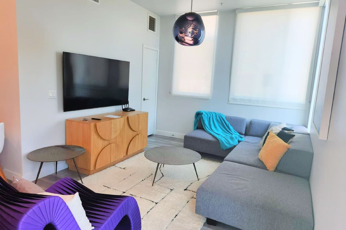 Un salon moderne avec un téléviseur à écran plat, un meuble en bois, un canapé gris et un fauteuil violet.