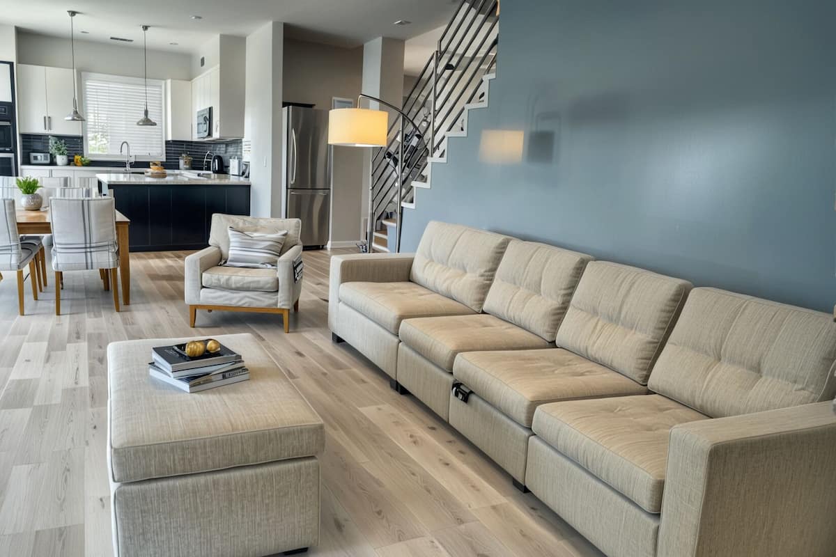 Un salon moderne comprenant un canapé, un pouf et un coin repas avec des chaises et une table.
