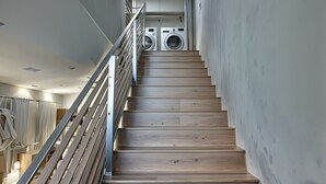 A staircase with wooden steps and metal railings leading to a laundry area with two washing machines. -  StaysPro - Hollywood Homes Minutes to Everything (Los Angeles)