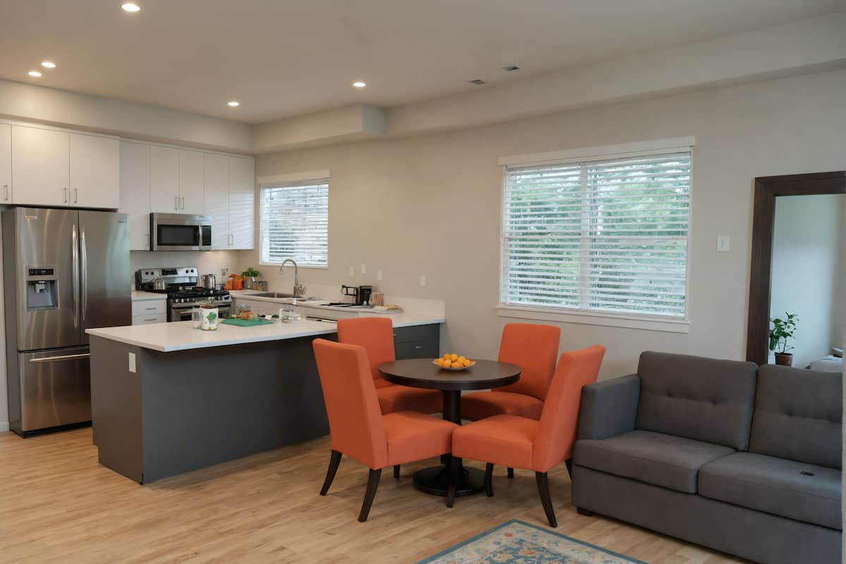 Une cuisine moderne avec un îlot central, un coin repas avec des chaises orange et un canapé gris.