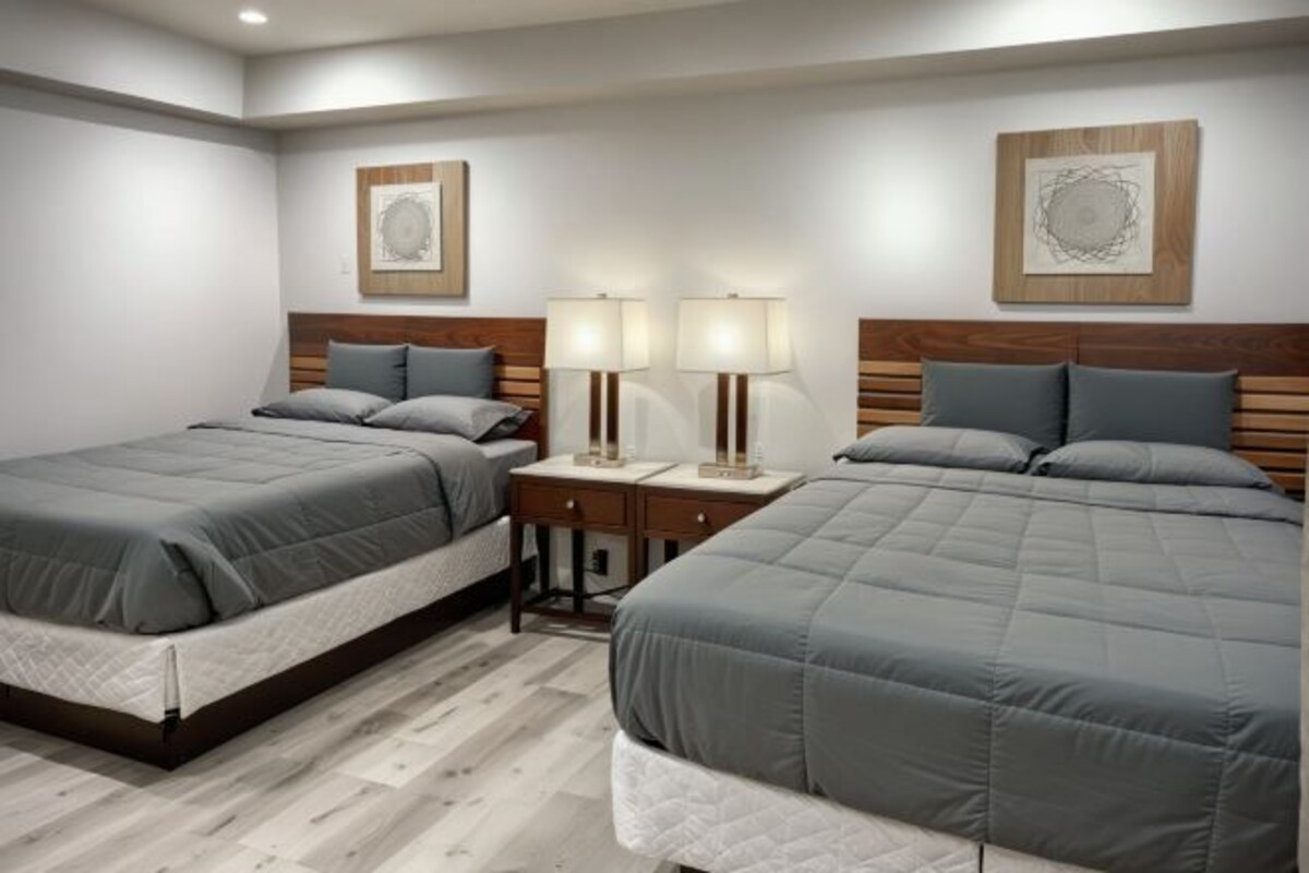 A hotel room with two beds, wooden headboards, bedside tables with lamps, and artwork on the walls.