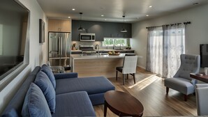 A modern kitchen with a central island, a dining area with a sofa and chairs, and a large window with curtains. -  StaysPro - Hollywood Homes Minutes to Everything (Los Angeles)