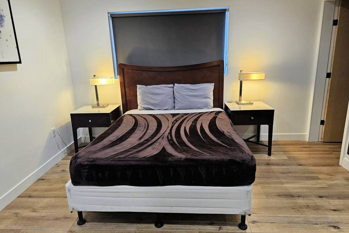 Une chambre à coucher comprenant un lit, deux tables de chevet, une commode, une tête de lit et un luminaire fixé au mur.