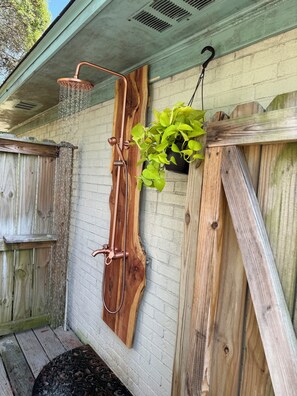 A wooden deck with a copper showerhead, a hanging plant, and a brick wall. - Seashell Cottage - 2 minute walk to private Bid-A-Wee Beach! NO  CROWDS! (Panama City Beach)