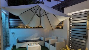 An outdoor patio area with white wicker furniture, a white umbrella, and a small table with decorative items. - Nice and elegant apartment in the center (Oliveri)