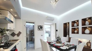 A modern kitchen with white cabinetry, a stainless steel range hood, and a dining area with a black table set for four. - Nice and elegant apartment in the center (Oliveri)