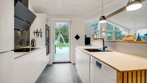 A modern kitchen with white cabinetry, a dishwasher, and a large window overlooking a deck.