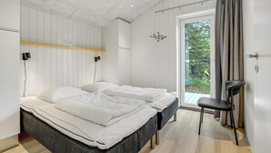 A modern bedroom with a bed, bedside tables, a chair, and a view of greenery through a glass door.