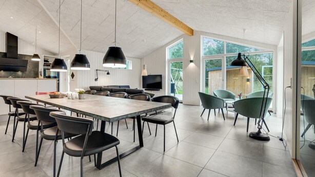 A modern kitchen with a large island, black pendant lights, and a dining area with chairs and a table.