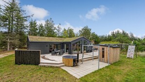 A modern cabin with a patio, outdoor seating, and a hot tub.