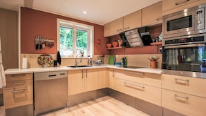 Une cuisine moderne avec des meubles en bois, des appareils électroménagers en acier inoxydable et une fenêtre qui laisse entrer la lumière naturelle.
