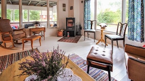 Un salon chaleureux avec une cheminée, des meubles en bois et de grandes fenêtres donnant sur l’extérieur.