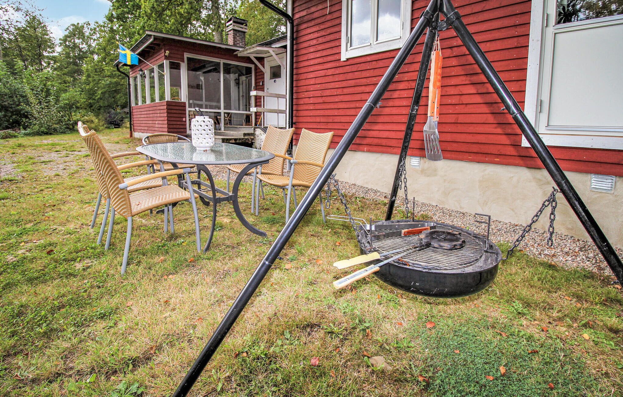 Ett rött hus med en veranda, ett runt glasbord med stolar och en grill.