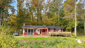 Une cabane rouge avec un porche, entourée du feuillage automnal.