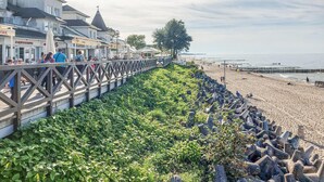 A coastal promenade with a wooden walkway, shops, and a beach.