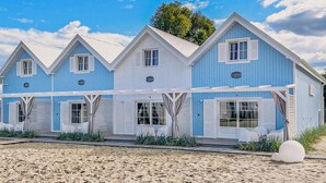 A coastal building with multiple gabled roofs, large windows, and a sandy foreground.