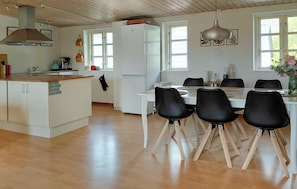 A modern kitchen with white cabinets, a wooden countertop, and a built-in oven. There is a dining area with a white table and black chairs.