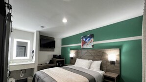 A modern hotel room with a large bed, a TV, a bathroom, and a green accent wall. - Bishop Arts Suites (Dallas)