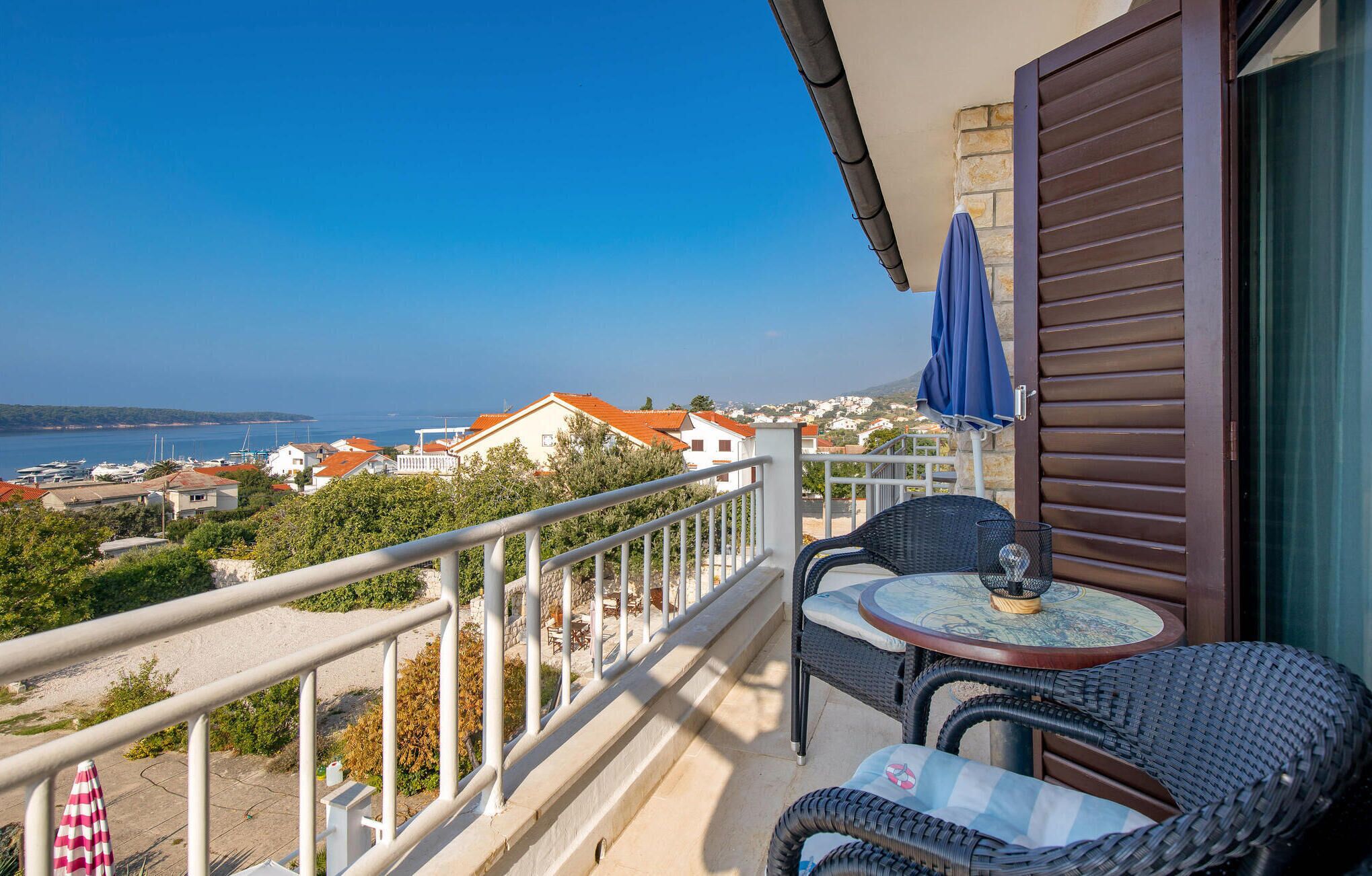 A balcony with wicker furniture, a table, and a view of the sea and buildings.