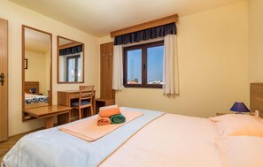 Quarto de hotel com cama, escrivaninha, cadeira, espelho, janela com cortinas e vista para o exterior.