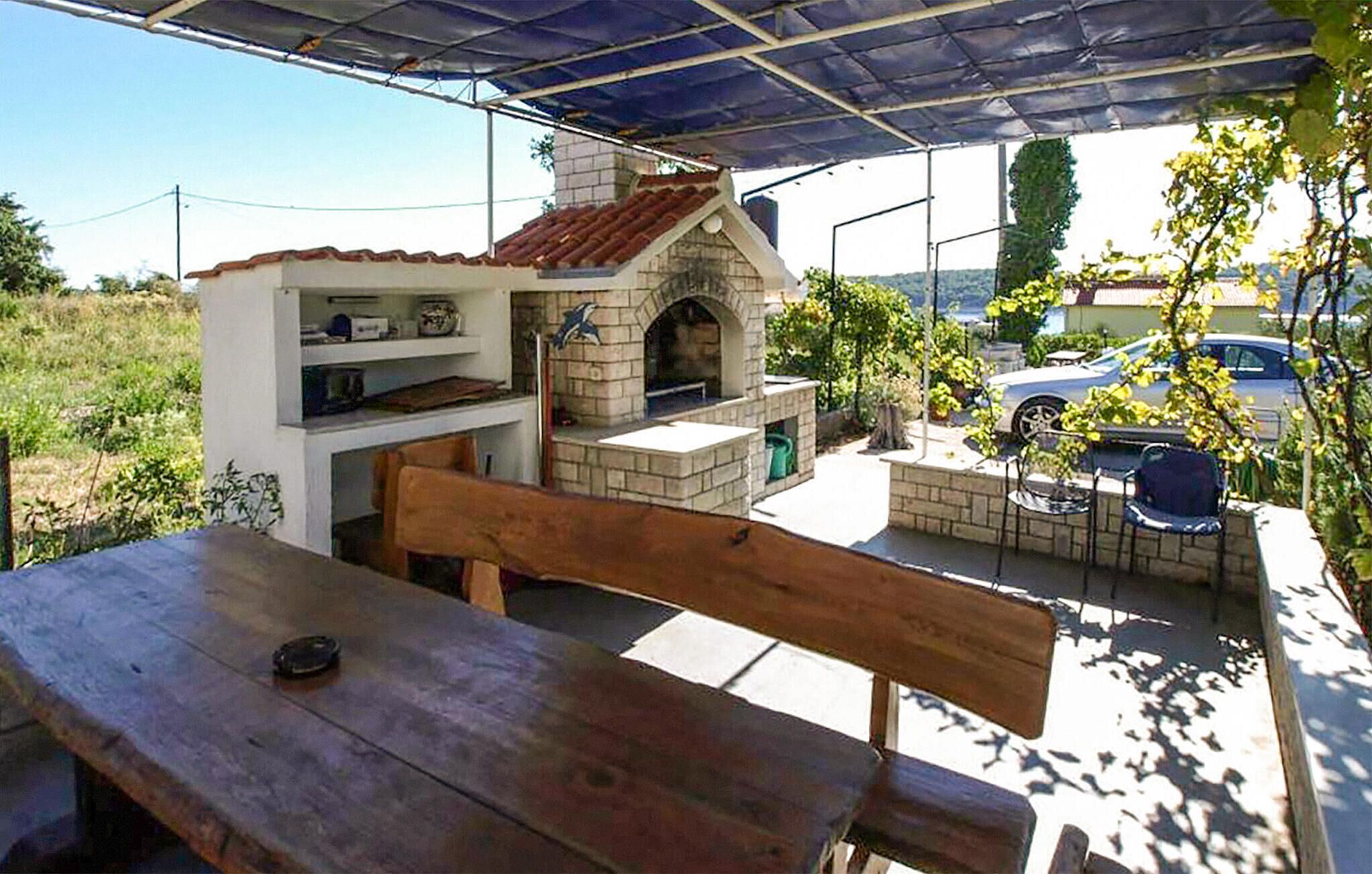 An outdoor patio with a brick-built barbecue area, a wooden table, and chairs.