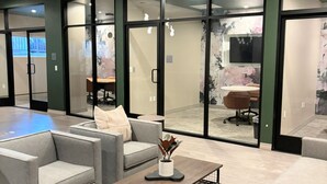 A modern office space with grey sofas, a coffee table, and a meeting room visible through glass doors. - StaysPro - GORGEOUS Hollywood Living Los Angeles (Los Angeles)