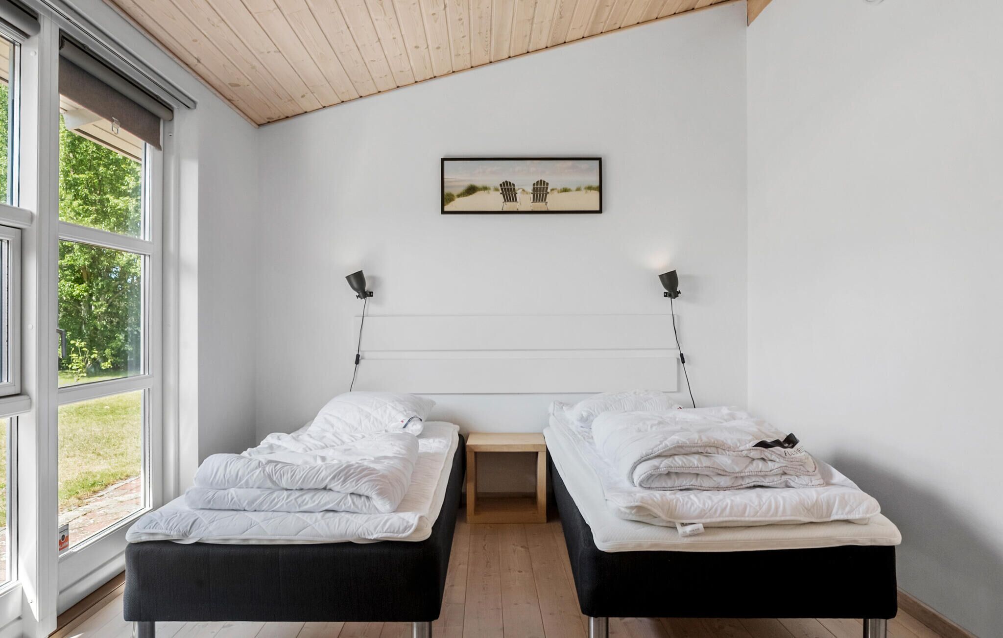 A bedroom with two beds, a wooden ceiling, and a framed picture on the wall.