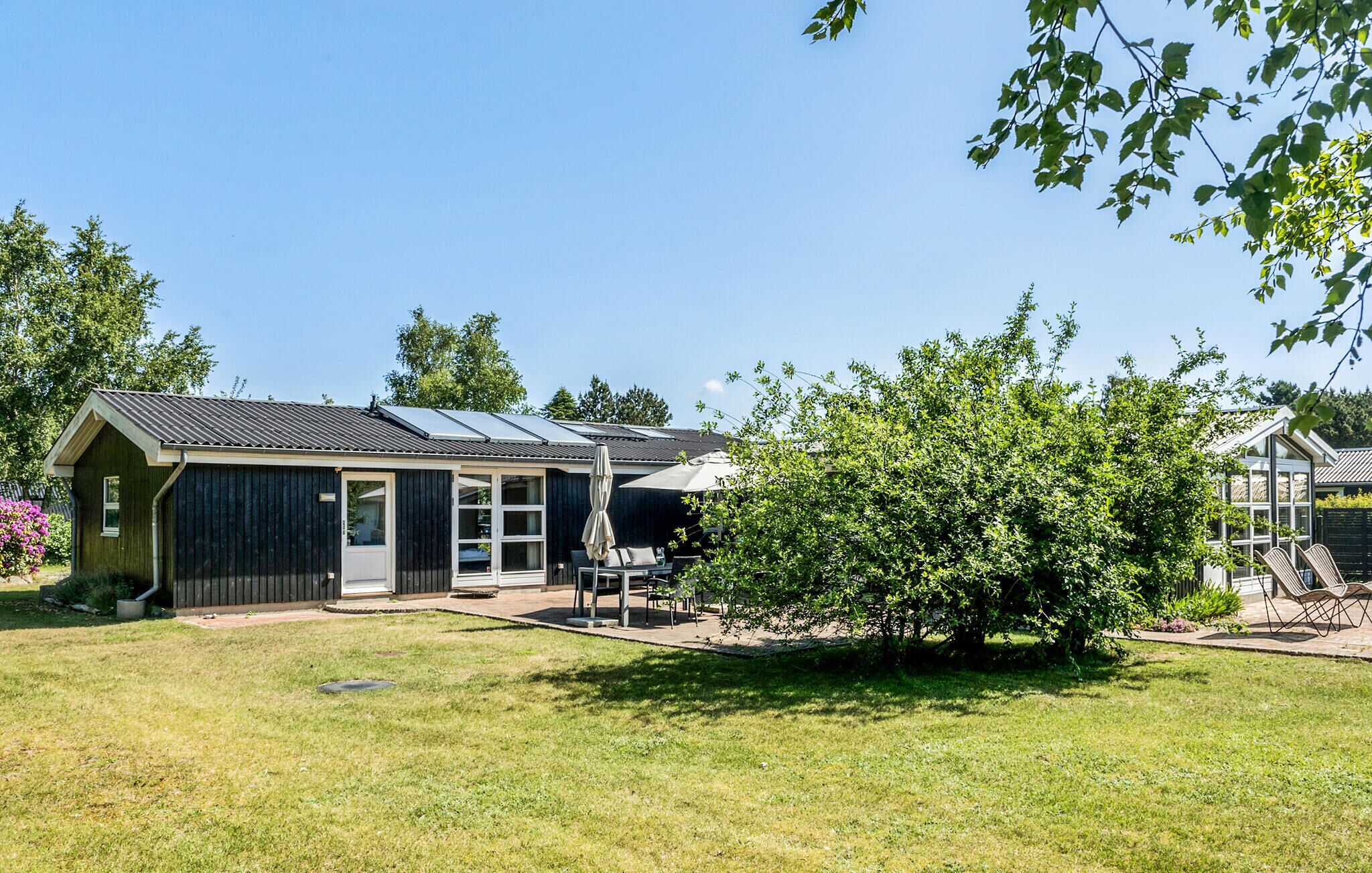 A single-story building with a dark exterior, a covered patio with outdoor seating, and solar panels on the roof.