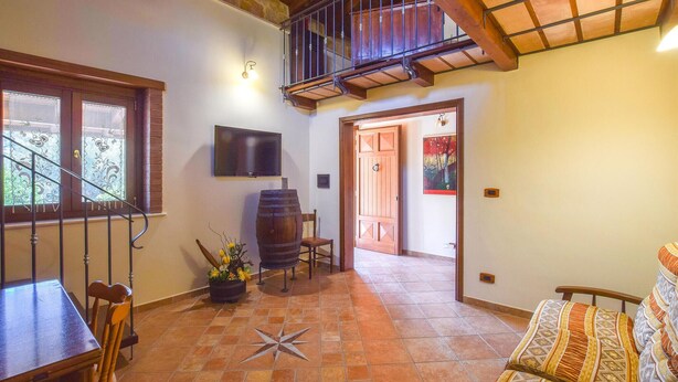 A spacious room with a tiled floor, a wooden dining table, a bar stool, a television mounted on the wall, and a staircase leading to an upper level. - Beautiful home in Reggio Calabria (Reggio Calabria)