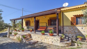 A yellow building with a stone foundation, a porch with a swing chair, and multiple potted plants. - Beautiful home in Reggio Calabria (Reggio Calabria)