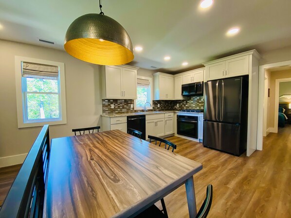 A modern kitchen with white cabinets, a stainless steel refrigerator, and a wooden dining table.