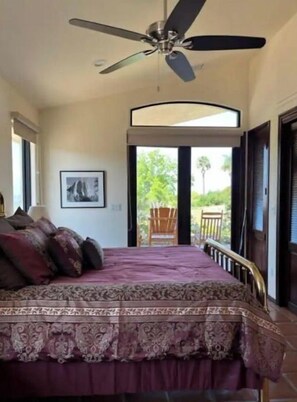 A bedroom with a bed, a ceiling fan, a window, and a door leading to an outdoor area.