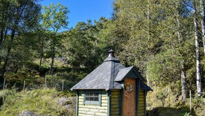 Pieni hirsihökkelö, jossa on jyrkkä katto ja savupiippu, ja sen ympärillä on tiheää metsää.