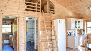 Puinen mökki, jonka sisätiloihin kuuluu keittiö, kylpyhuone ja parvelle sijoitettu makuuhuone.