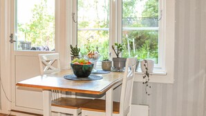 A dining area with a wooden table, white chairs, and a window with a view of greenery.