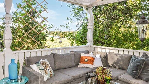 A covered outdoor seating area with a cushioned sofa, a small table, and decorative items.