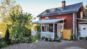 A red wooden house with a porch, a garage, and a garden with various plants.