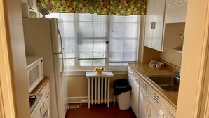 A compact kitchen with white cabinets, a microwave, a stove, a sink, and a window with blinds.