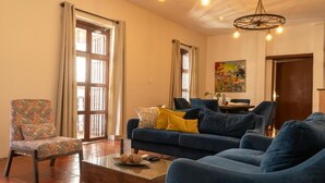 A living room with a sofa, armchairs, a coffee table, and a patterned armchair. There are curtains on the windows, a painting on the wall, and a chandelier. - old City 5br Piscina Rooftop AC hot Water (Cartagena de Indias)