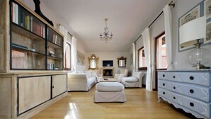 Ein geräumiges Zimmer mit Holzboden, weißen Möbeln, einem Chandelier und einem Bücherregal.