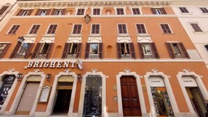 Ein Gebäude mit der Aufschrift "BRIGHTEN" an der Fassade, ausgestattet mit zahlreichen Fenstern mit Fensterläden, einem zentralen Eingang und verschiedenen Geschäften mit sichtbarer Beschilderung.