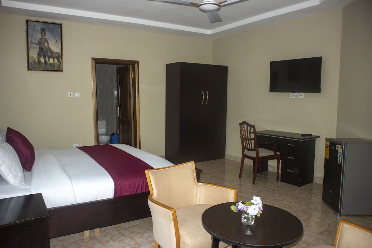 Habitación de hotel con cama, escritorio, silla, televisor y un refrigerador pequeño.