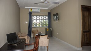 Una habitación con ventilador de techo, aire acondicionado, una mesa de comedor con sillas, un refrigerador y una puerta de madera.